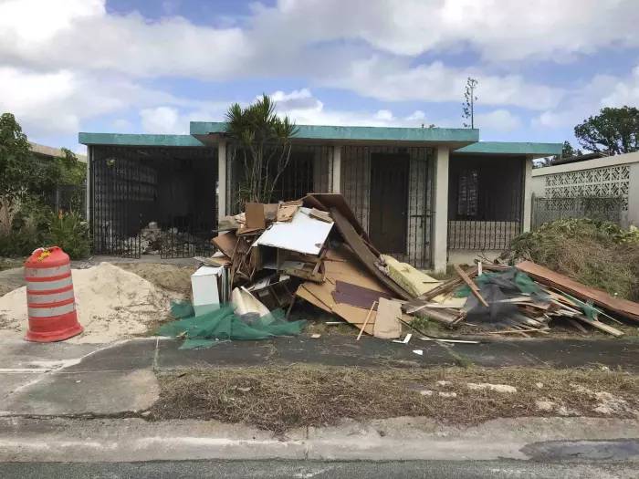 Casa de una planta con escombros al frente en Puerto Rico, propiedad que necesita reparaciones