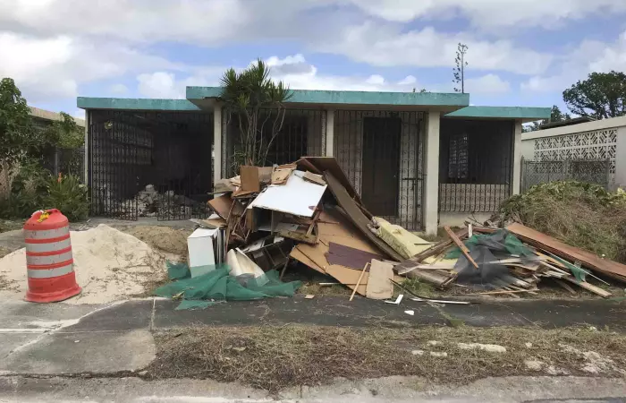 Casa de una planta con escombros al frente en Puerto Rico, propiedad que necesita reparaciones