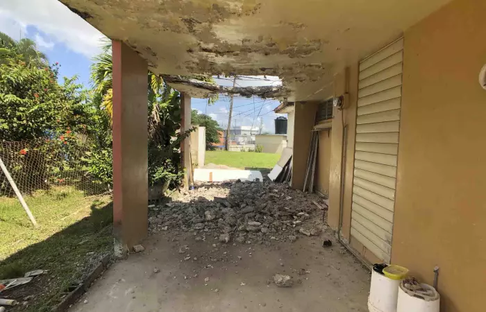 Marquesina con techo de hormigón deteriorado y escombros, casa con daños estructurales