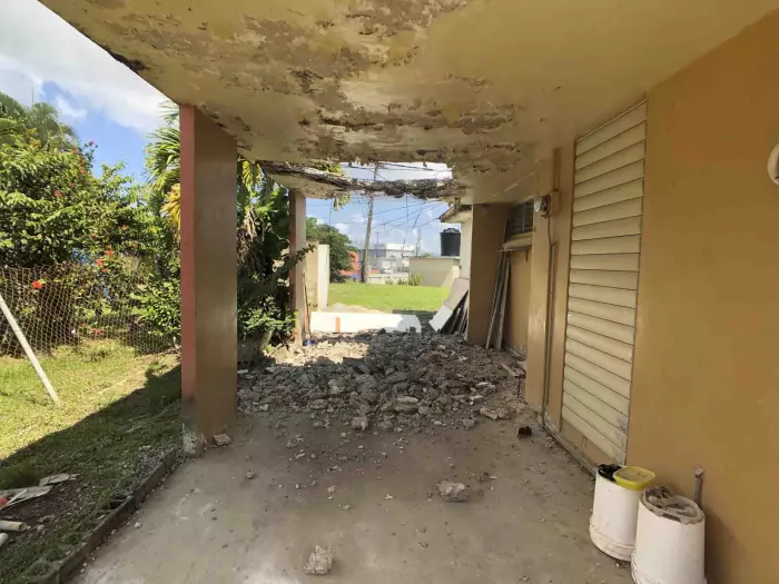 Marquesina con techo de hormigón deteriorado y escombros, casa con daños estructurales