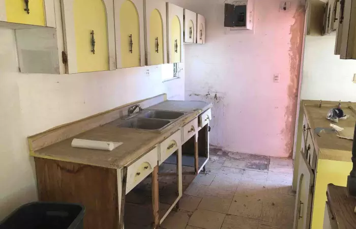 Cocina antigua con gabinetes amarillos desgastados en una casa sin remodelar