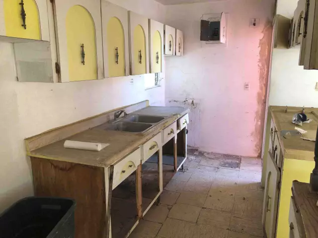 Cocina antigua con gabinetes amarillos desgastados en una casa sin remodelar