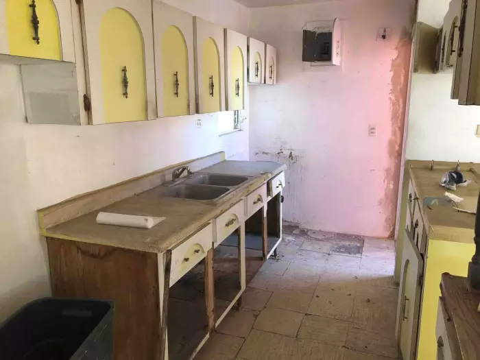 Cocina antigua con gabinetes amarillos desgastados en una casa sin remodelar