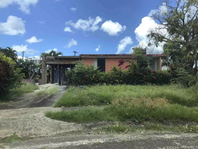 Casa con patio de hierba crecida y estructura en obra en Puerto Rico, propiedad en cualquier condición