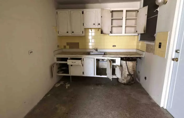 Cocina desmantelada con gabinetes abiertos y losas amarillas, casa para remodelar