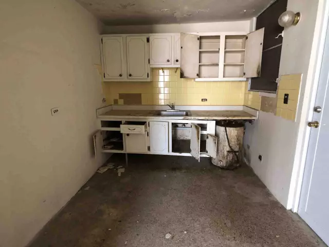 Cocina desmantelada con gabinetes abiertos y losas amarillas, casa para remodelar