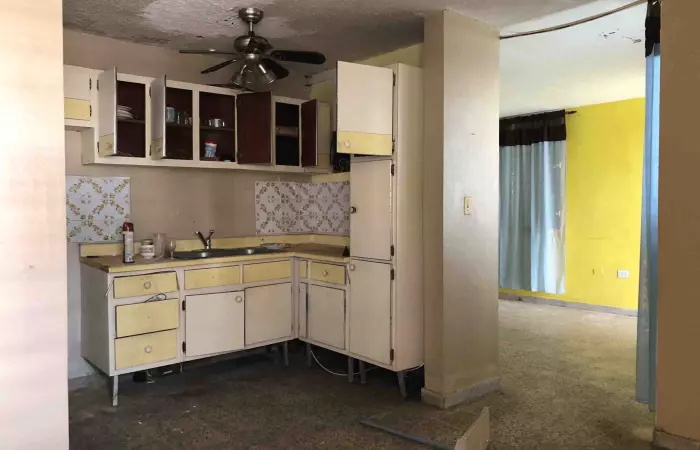 Cocina antigua sin actualizar junto a sala con pared amarilla en una casa desocupada