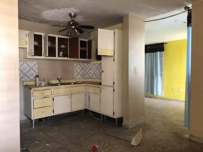 Cocina antigua sin actualizar junto a sala con pared amarilla en una casa desocupada