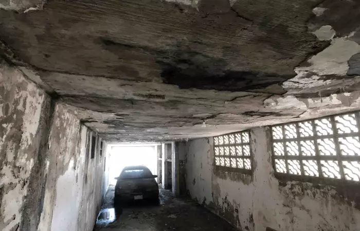 Garaje con techo de hormigón muy deteriorado y auto abandonado, casa con problemas estructurales