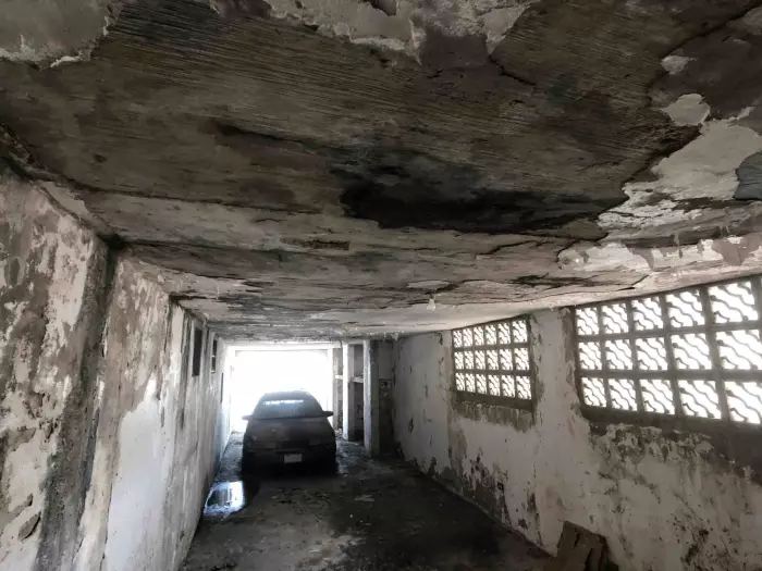 Garaje con techo de hormigón muy deteriorado y auto abandonado, casa con problemas estructurales