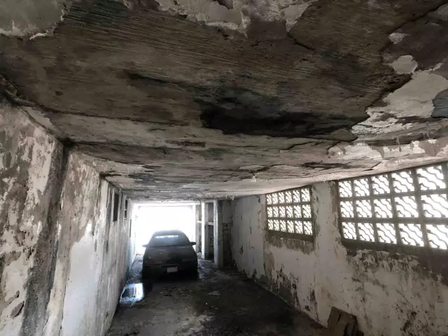 Garaje con techo de hormigón muy deteriorado y auto abandonado, casa con problemas estructurales